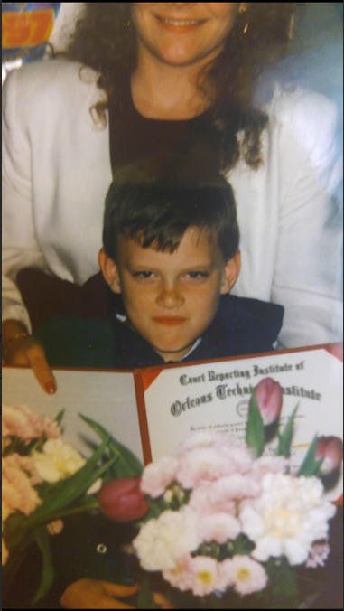 Mike as a child beside his mother, holding her court reporting diploma among graduation flowers in 1996. The original photograph crops the top of her face.